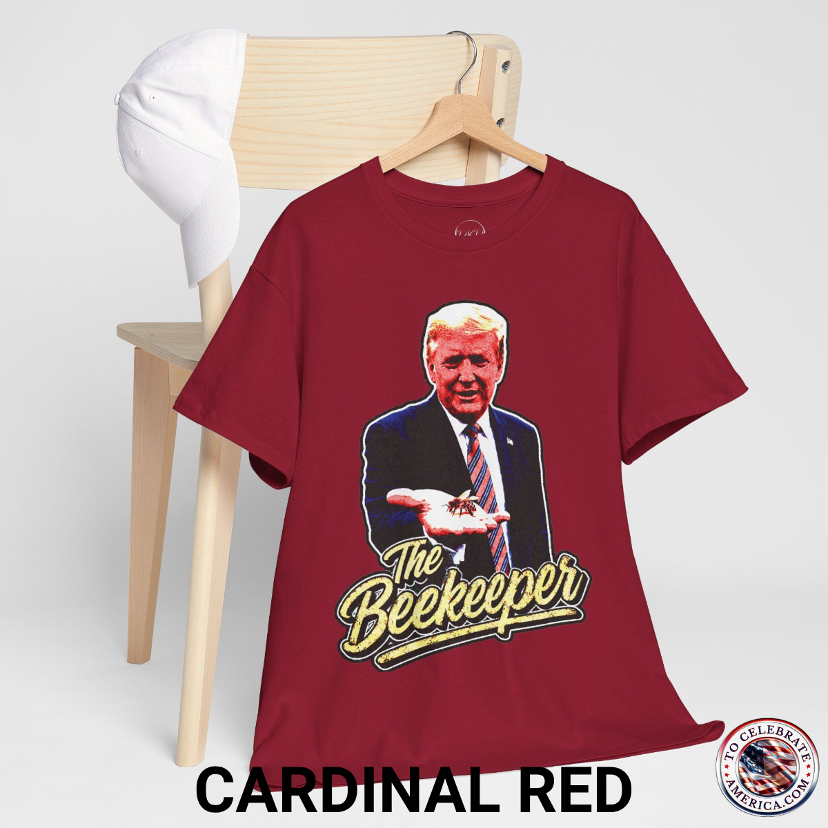 Cardinal Red T‑shirt featuring a pop‑art grunge illustration of President Trump holding a bee in his hand with bold ‘The Beekeeper’ text below.