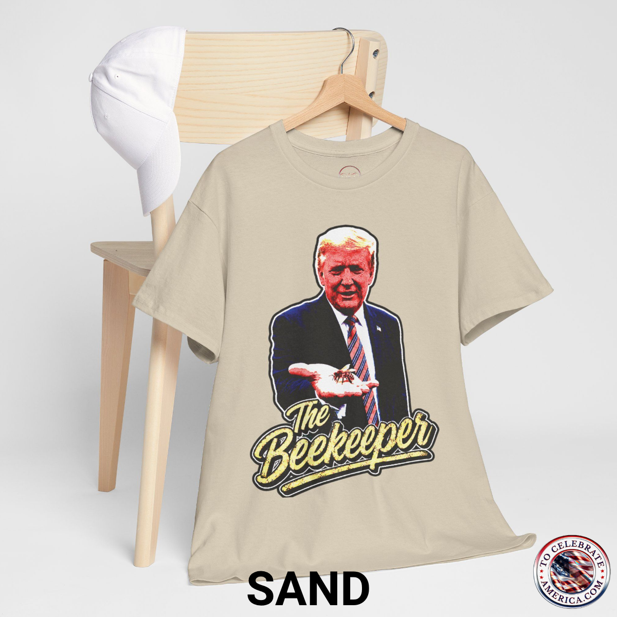 Sand Color T‑shirt featuring a pop‑art grunge illustration of President Trump holding a bee in his hand with bold ‘The Beekeeper’ text below.
