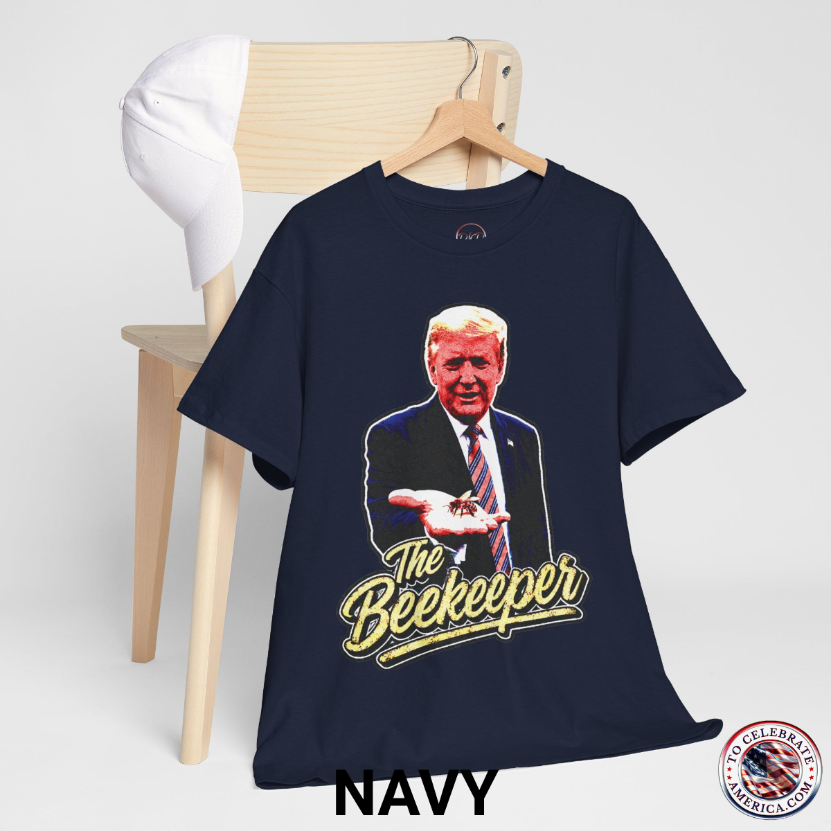 Navy T‑shirt featuring a pop‑art grunge illustration of President Trump holding a bee in his hand with bold ‘The Beekeeper’ text below.
