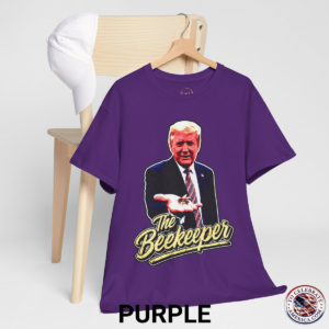 Purple T‑shirt featuring a pop‑art grunge illustration of President Trump holding a bee in his hand with bold ‘The Beekeeper’ text below.
