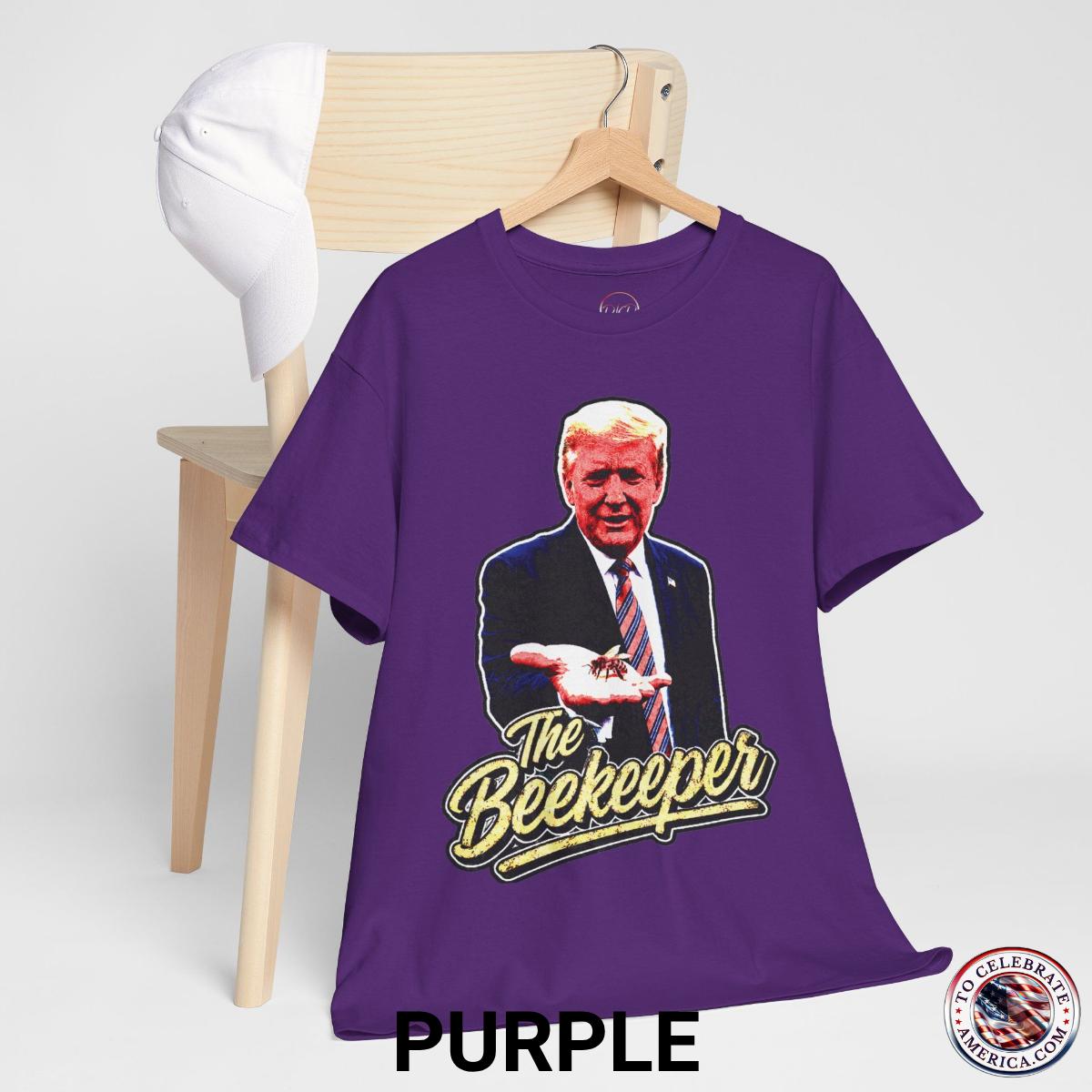Purple T‑shirt featuring a pop‑art grunge illustration of President Trump holding a bee in his hand with bold ‘The Beekeeper’ text below.