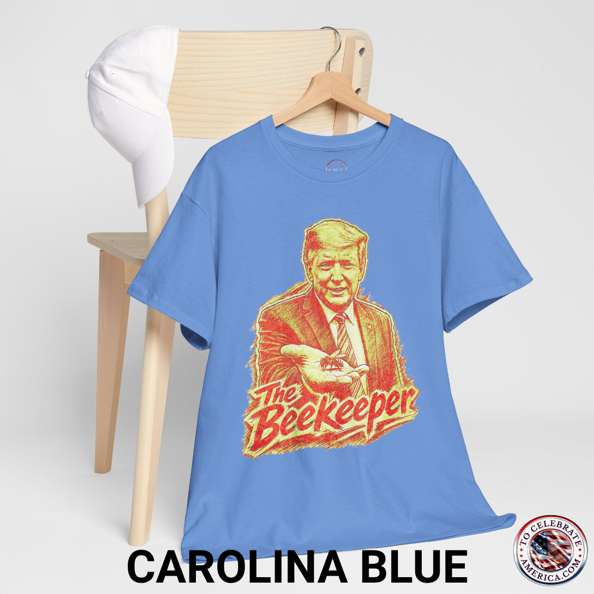 Carolina Blue T‑shirt featuring a pencil‑sketch illustration of President Trump holding a small bee in an outstretched hand, with stylized ‘The Beekeeper’ text below.