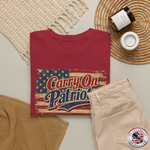 Antique Cherry Red T‑shirt featuring distressed American flag background with bold ‘Carry On Patriots’ vintage lettering. Set against feminine wearing apparel featuring a straw summer hat knitted scarf, slacks, and sunscreen